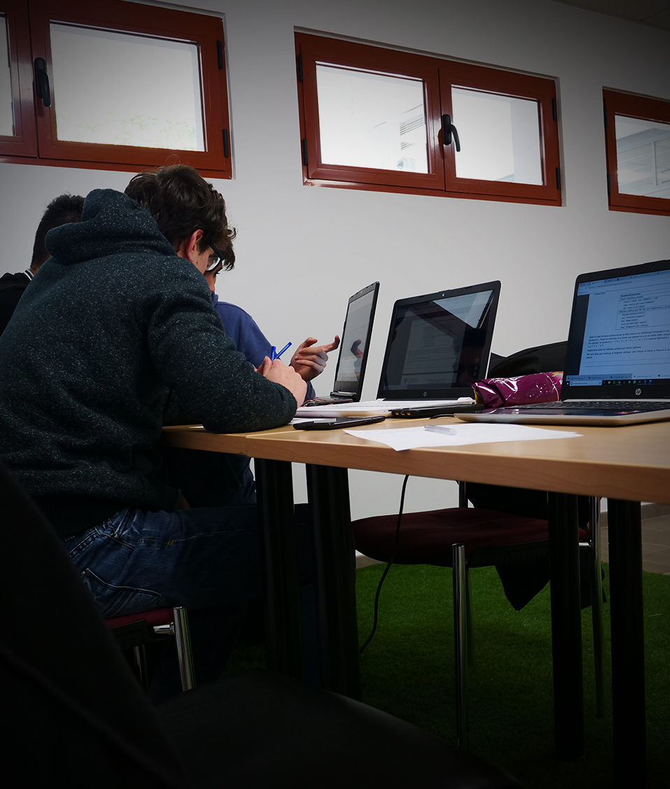 Un grupo de alumnos hablando y estudiando en una mesa con varios ordenadores